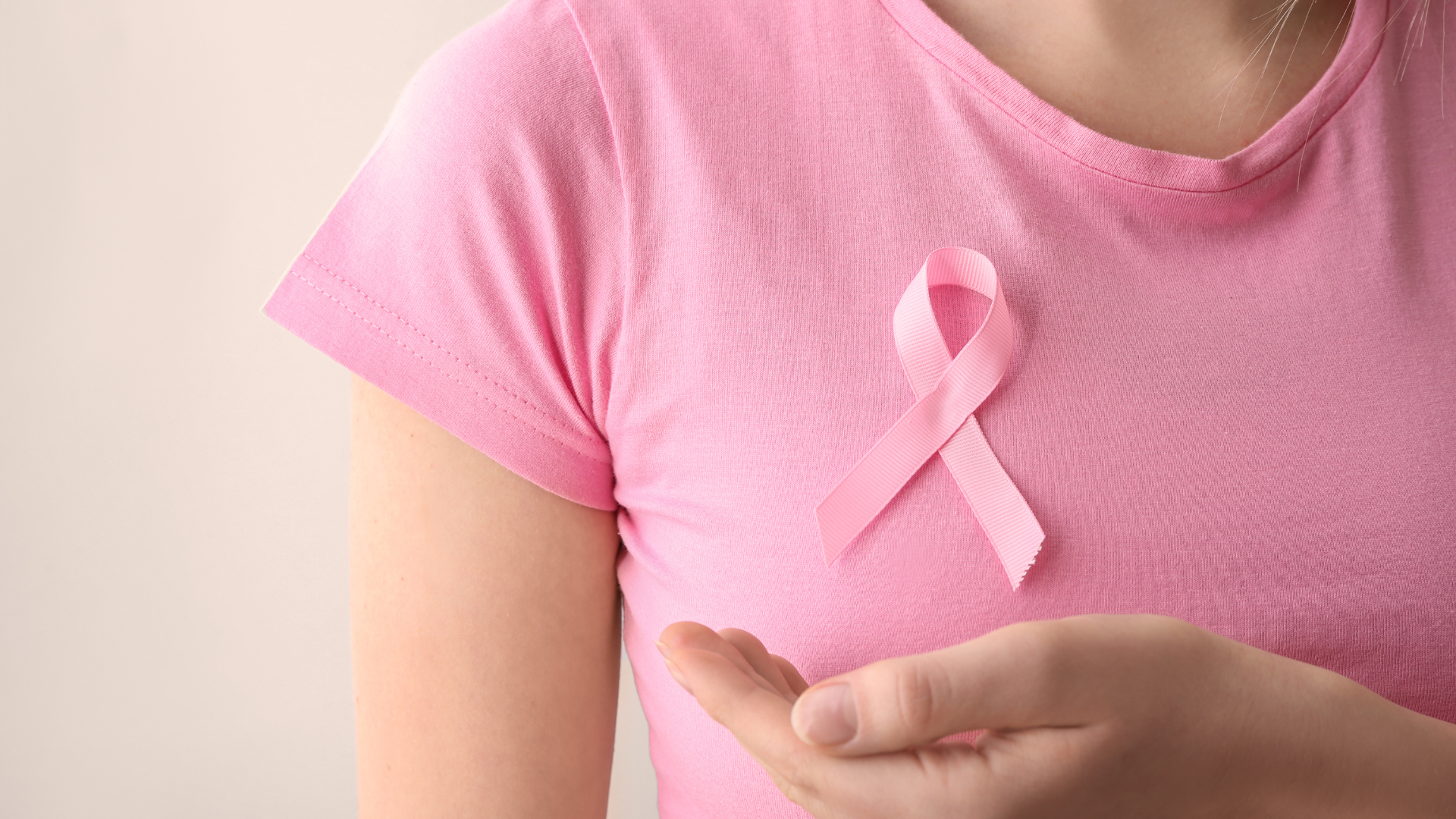 Foto de uma mulher com camiseta rosa e faixa da campanha outubro rosa